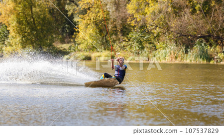 Young wakeboarder surfing along the river 107537829