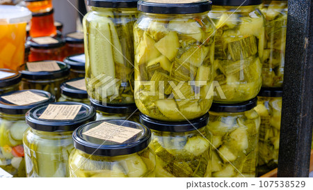 Canned vegetables, zucchini cut pieces with spices in glass jars on kitchen table during home canning, fragment close-up Canned vegetables, zucchini cut pieces with spices in glass jars on kitchen table during home canning, fragment close-up 107538529