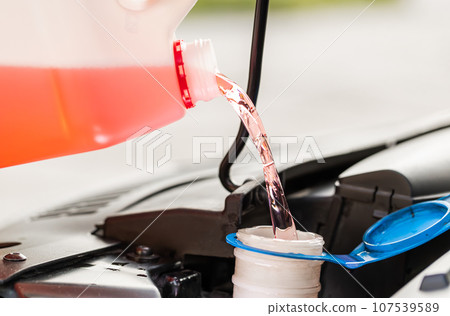 Service worker man pours car fluid windscreen red cleaning washer glass summer or winter cleaner Service worker man pours car fluid windscreen red cleaning washer glass summer or winter cleaner 107539589