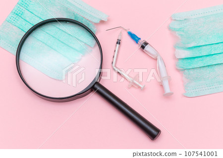 Broken Medical Syringe and Green Torn Medical Face Mask with Magnifying Glass 107541001
