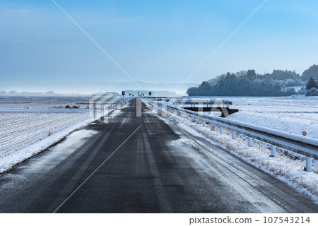 A straight farm road in a snowy landscape during the bitterly cold season A straight farm road in a snowy landscape during the bitterly cold season 107543214
