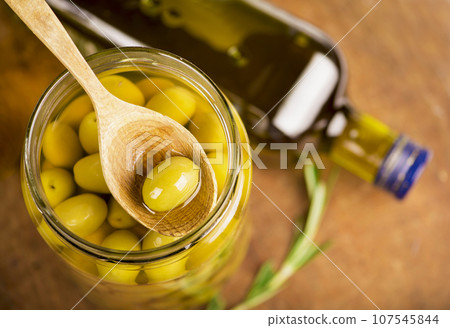 Close up green olives in wooden spoon, rosemary on a wooden background 107545844