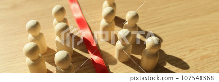 Small wooden figurines separated by red ribbon on table 107548368
