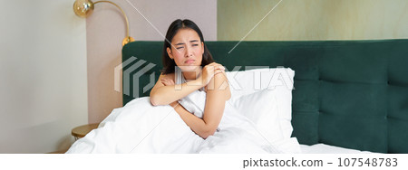 Portrait of asian teen girl lying in bed and grimacing, unwilling to wake up, looking outside window with frowned, reluctant face Portrait of asian teen girl lying in bed and grimacing, unwilling to wake up, looking outside window with frowned, reluctant face 107548783