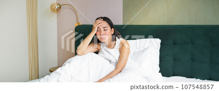 Portrait of sad young woman waking up, feeling bad, wants to sleep, wakes early morning, looking lazy and upset 107548857