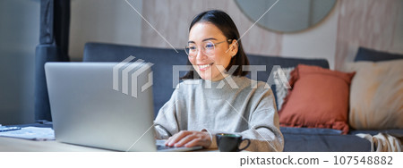 Portrait of asian businesswoman smiling, working on laptop from home, remote online studying in her living room 107548882