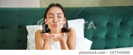 Beautiful korean girlfriend, girl in bed, sending air kiss at camera, lying in bed in her bedroom, waking up early 107548900