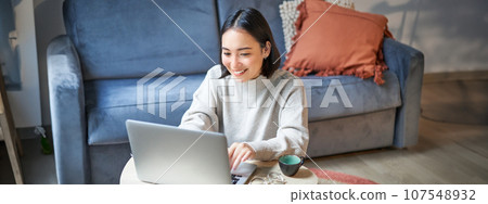 Beautiful asian girl works from home, studying with laptop, sitting in living room, being on remote, freelancing online Beautiful asian girl works from home, studying with laptop, sitting in living room, being on remote, freelancing online 107548932