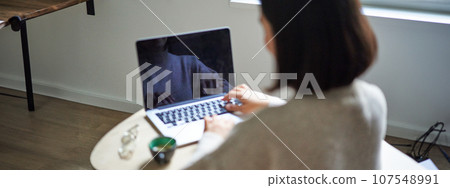 Rear view of woman, typing and working on laptop, computer screen is empty for copy space, female student studying remotely 107548991