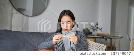 Shocked woman looks concerned at her thermometer, catching cold, has fever, sitting on sick leave at home 107549047