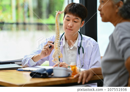 Orthopedist giving consultation about scoliosis or spinal problems to mature female patient during medical exam Orthopedist giving consultation about scoliosis or spinal problems to mature female patient during medical exam 107551936