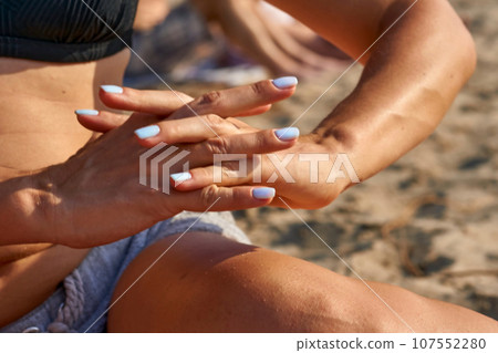 Woman hands on knees with a beautiful blue manicure on a sunny day at the beach 107552280