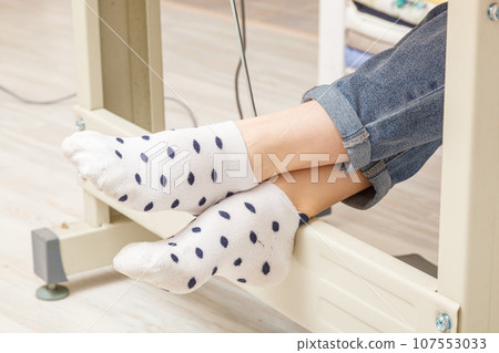 Female feet on the pedal of a sewing machine, motor 107553033