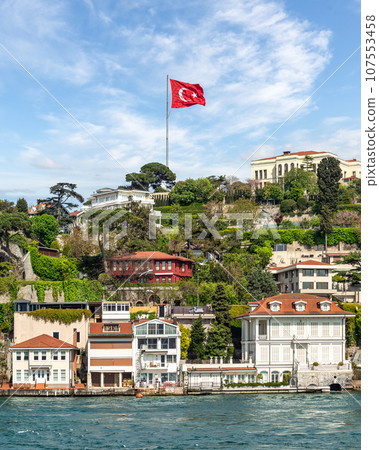 White houses on a green hill by Bosphorus in Istanbul, Turkey, with a large Turkish flag flying overhead White houses on a green hill by Bosphorus in Istanbul, Turkey, with a large Turkish flag flying overhead 107553458