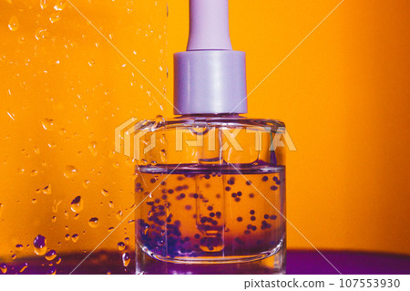Hyaluronic acid in a glass bottle with a pipette on an orange background against wet glass. Facial Serum or cuticle oil in a bathroom. Hydro boost serum provides active moisturizing for aging skin. 107553930