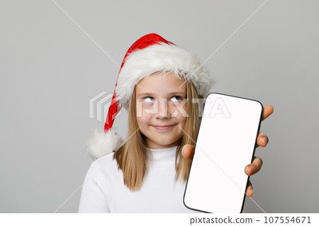 Cute Christmas kid Santa hat looking up holding smartphone with blank empty white screen display 107554671