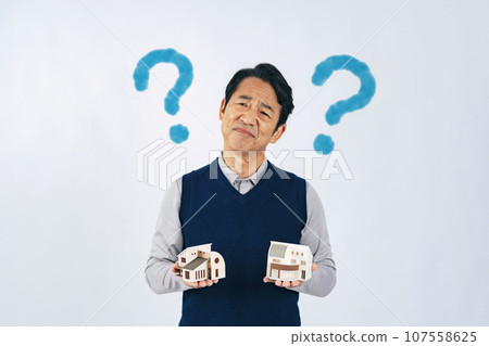 A middle-aged man holding a house model and worrying 107558625