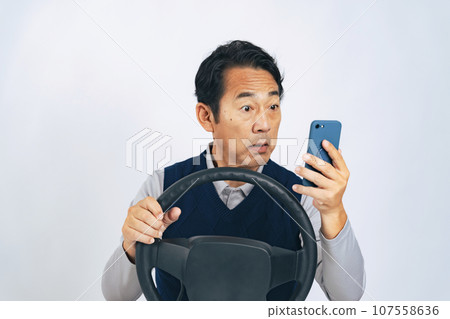 Middle-aged man looking at smartphone while driving Middle-aged man looking at smartphone while driving 107558636