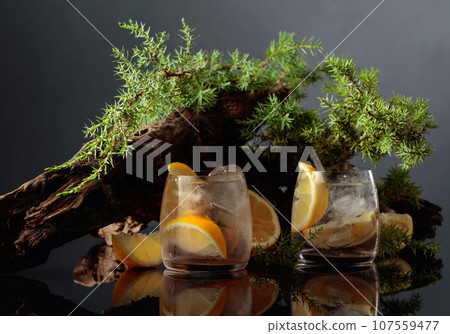 Cocktail gin-tonic with ice and lemon on a black reflective background. Cocktail gin-tonic with ice and lemon on a black reflective background. 107559477