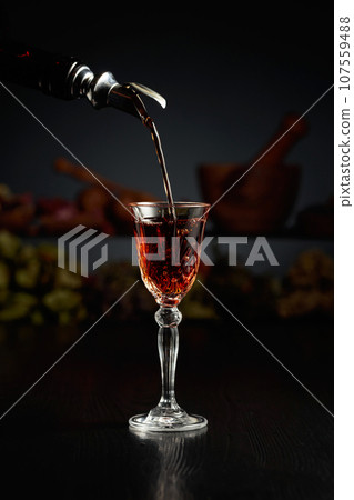 Brown herbal liquor or rum is poured from a vintage bottle. 107559488