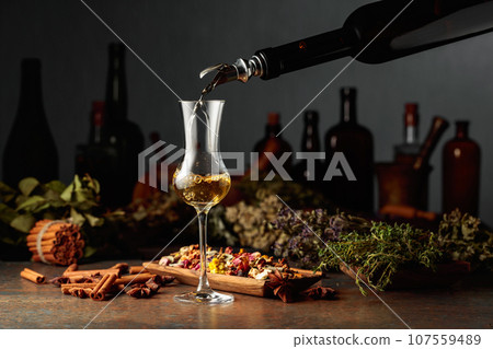 Yellow herbal liquor or balm is poured from a vintage bottle into a glass. 107559489