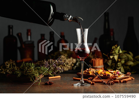 Brown herbal liquor or balm is poured from a vintage bottle into a glass. Brown herbal liquor or balm is poured from a vintage bottle into a glass. 107559490