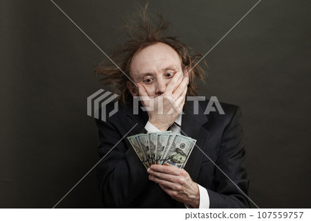 Stressed businessman holding 100 US dollar banknote cash money on black background, studio portrait Stressed businessman holding 100 US dollar banknote cash money on black background, studio portrait 107559757