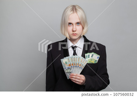 Young serious businesswoman in formal suit with euro banknote holding US dollar money bill Young serious businesswoman in formal suit with euro banknote holding US dollar money bill 107560032