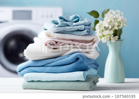 Washing machine with clothes stacked for laundry day. Pile of clothes next to a washing machine on pastel background Washing machine with clothes stacked for laundry day. Pile of clothes next to a washing machine on pastel background 107560195