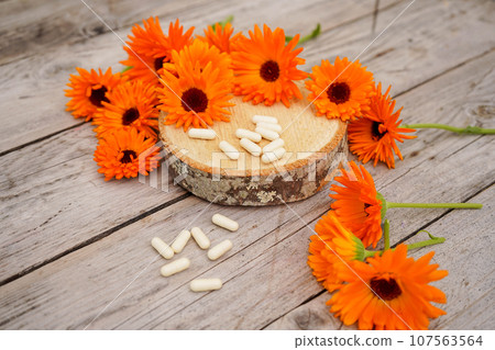 Calendula alternative medicine. White pills on a wooden table, fresh blooming calendula background, 107563564