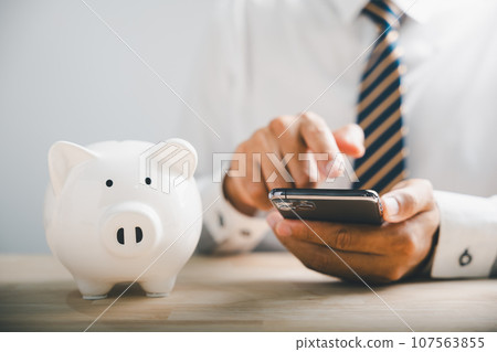 Saving money in piggybank. Mobile banking and budgeting concept with smartphone. Growing fund on white desk. Financial support banner. white background. Financial Money Advice 107563855