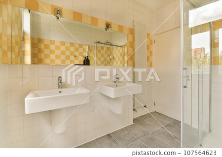 a bathroom with yellow and white tiles on the walls, two sinks and a shower stall in front of it a bathroom with yellow and white tiles on the walls, two sinks and a shower stall in front of it 107564623