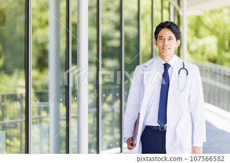 一位身穿白大褂的年輕男醫生沿著醫療機構的走廊行走 107566582