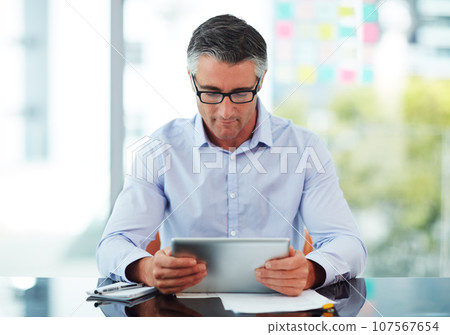 Connected to the corporate world. Cropped shot of a mature businessman working on his tablet in the office. 107567654