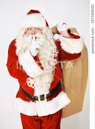 Secret, quiet and santa with christmas gift sack for silent holiday present giving in red suit. Silence of santa claus model holding festive gifts bag in studio with white background thinking. Secret, quiet and santa with christmas gift sack for silent holiday present giving in red suit. Silence of santa claus model holding festive gifts bag in studio with white background thinking. 107568085
