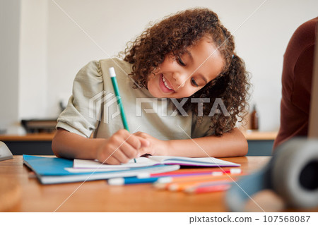 Learning, smiling and creative young girl drawing with a colorful pencil feeling happy and content. Positive student with a smile having a fun time creating artistic art in her kids notebook at home 107568087