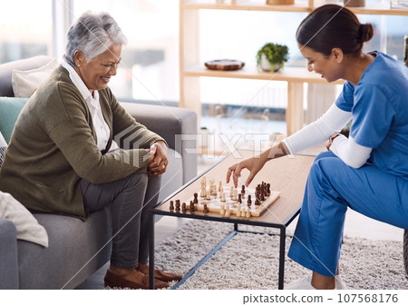 Women, chess and nurse with a senior patient, retirement home and happiness with healthcare. Female person, medical professional and mature lady with employee, nursing and care with games and relax 107568176