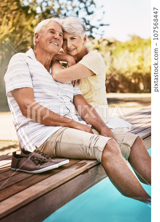 Senior couple, relax and smile for pool, love and summer vacation, bonding or quality time together in the outdoors. Happy elderly man and woman relaxing and hugging with feet in water by a poolside 107568447