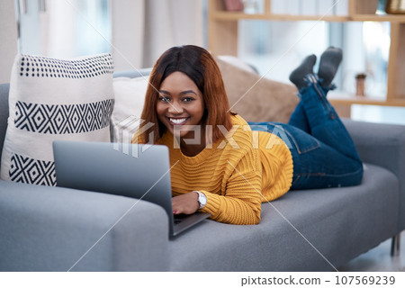 Black woman with laptop, portrait and relax on sofa, search online for movie and streaming subscription at home. Happy African female person in apartment, connectivity and watching on pc with web 107569239