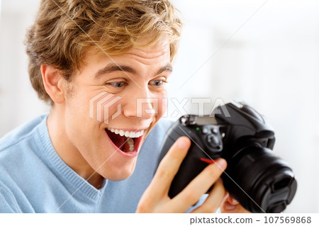 Risks do pay off. Shot of a young man using his digital camera at home. 107569868