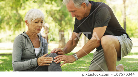 Old couple, woman with knee pain and injury in park, fibromyalgia health problem and joint ache from exercise. Man helping, arthritis and people in retirement with fitness outdoor and muscle tension 107570344