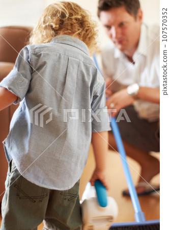 Boy, dad and vacuum cleaner on floor together with learning, support or cleaning in family home with care. Man, male child and teaching life skills with love, broom and development for clean flooring 107570352