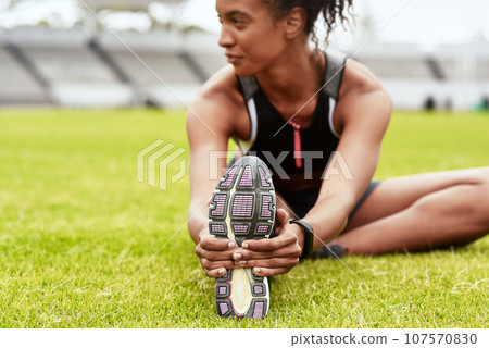 Woman, hands and athlete stretching legs on grass at stadium in preparation for running, exercise or workout. Active or fit female person in warm up leg stretch for fitness, sports or run on field 107570830