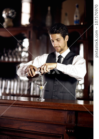 Bartender man, glass and mixing cocktail at bar for service, drink or hospitality at party, club or event. Male server, barman or waiter with alcohol, spirit or mixer for presentation at restaurant 107570970