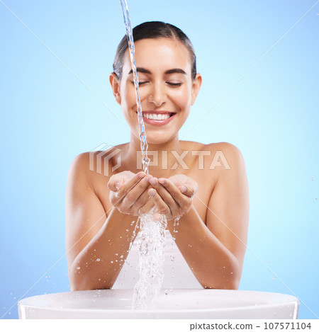 Woman, hands and water splash with smile for skincare hygiene, wash or facial treatment in sink against blue studio background. Happy female smiling in natural beauty cleanse, minerals or self care Woman, hands and water splash with smile for skincare hygiene, wash or facial treatment in sink against blue studio background. Happy female smiling in natural beauty cleanse, minerals or self care 107571104