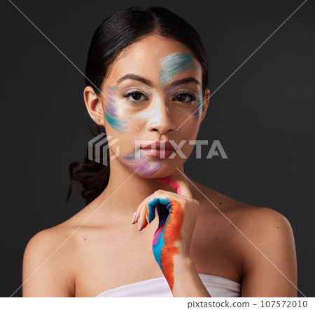 Beauty, portrait and woman with paint art on hand and face in studio. Creative skin and rainbow makeup on serious female aesthetic model on gray background for lgbtq color inspiration on hands 107572010