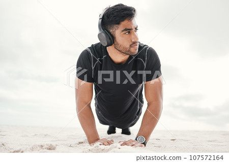 Your workouts can be fun, just add music. a sporty young man wearing headphones while doing push ups on the beach. 107572164