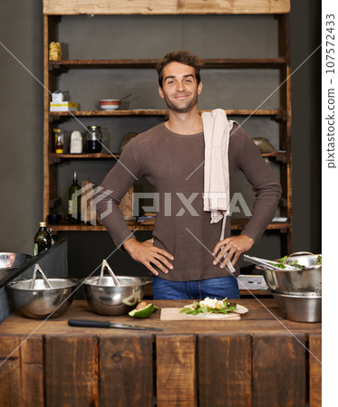 Chef, man akimbo and portrait in kitchen while making delicious food for healthy diet and nutrition. Cooking, confidence and male cook standing in rustic restaurant or small business in Canada. 107572433