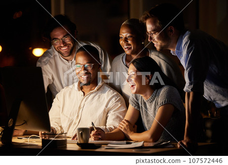 Glad to see everything coming together so well. Shot of a group of businesspeople working together on a computer in an office at night. 107572446