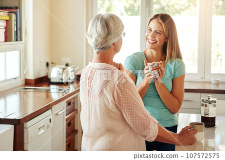 Mother, coffee or happy woman laughing in kitchen in family home bonding or enjoying quality time together. Speaking, retirement or funny girl talking, relaxing or drinking tea with senior parent 107572575